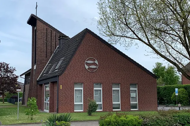 Moderne Backsteinkirche mit markantem Kreuz und Fischsymbol.