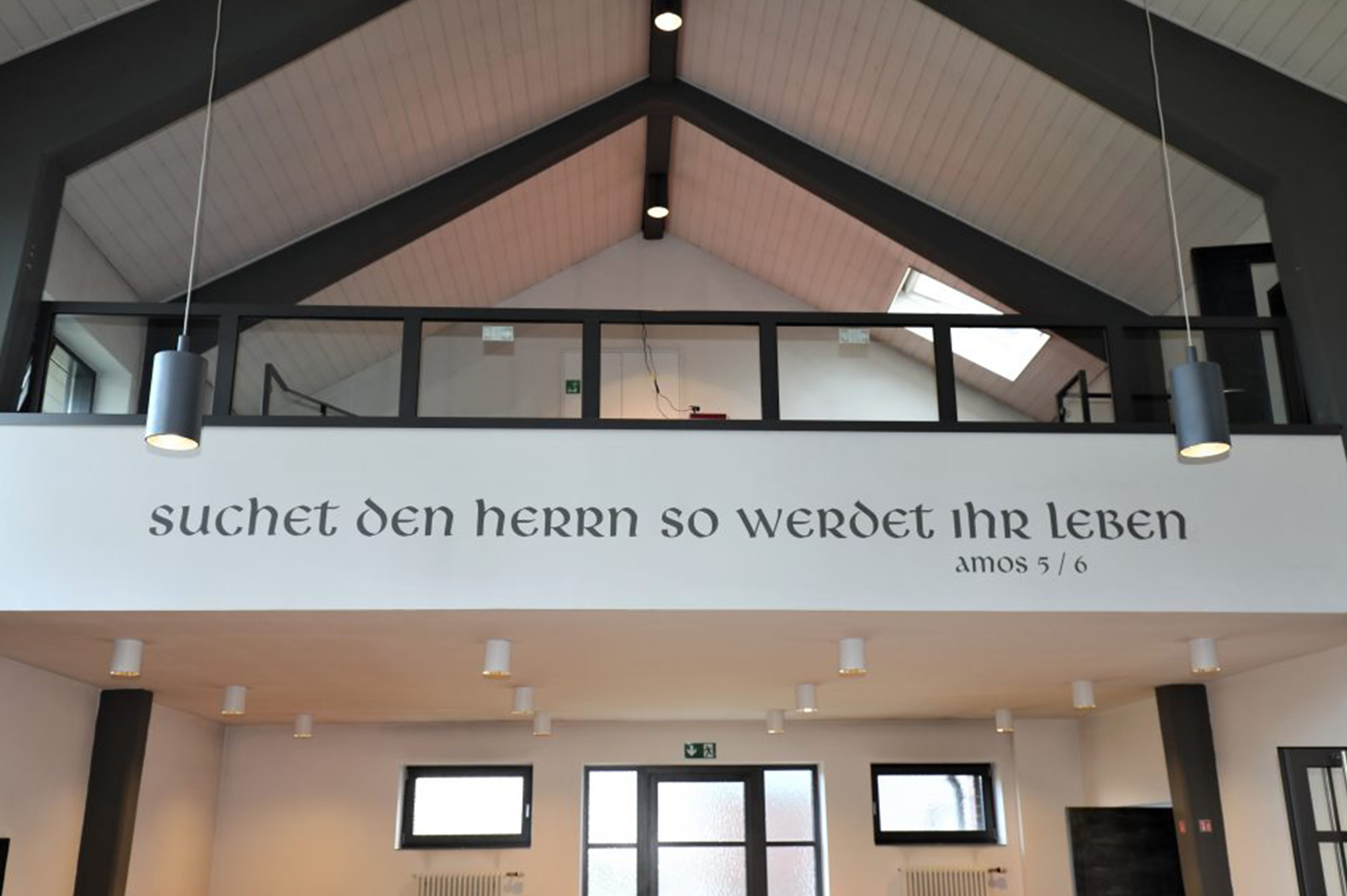 Kircheninnenraum mit deutschem Schriftzug "Amos 5/6" und Empore.