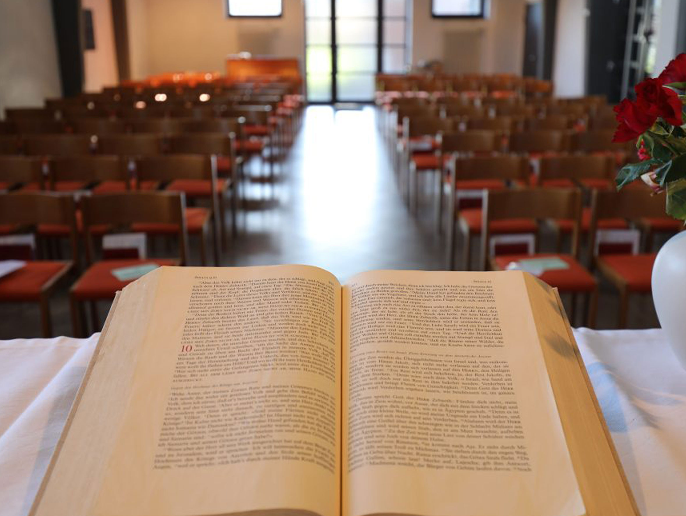 Offenes Buch auf Altar, leere Kirchenbänke in Reihen.