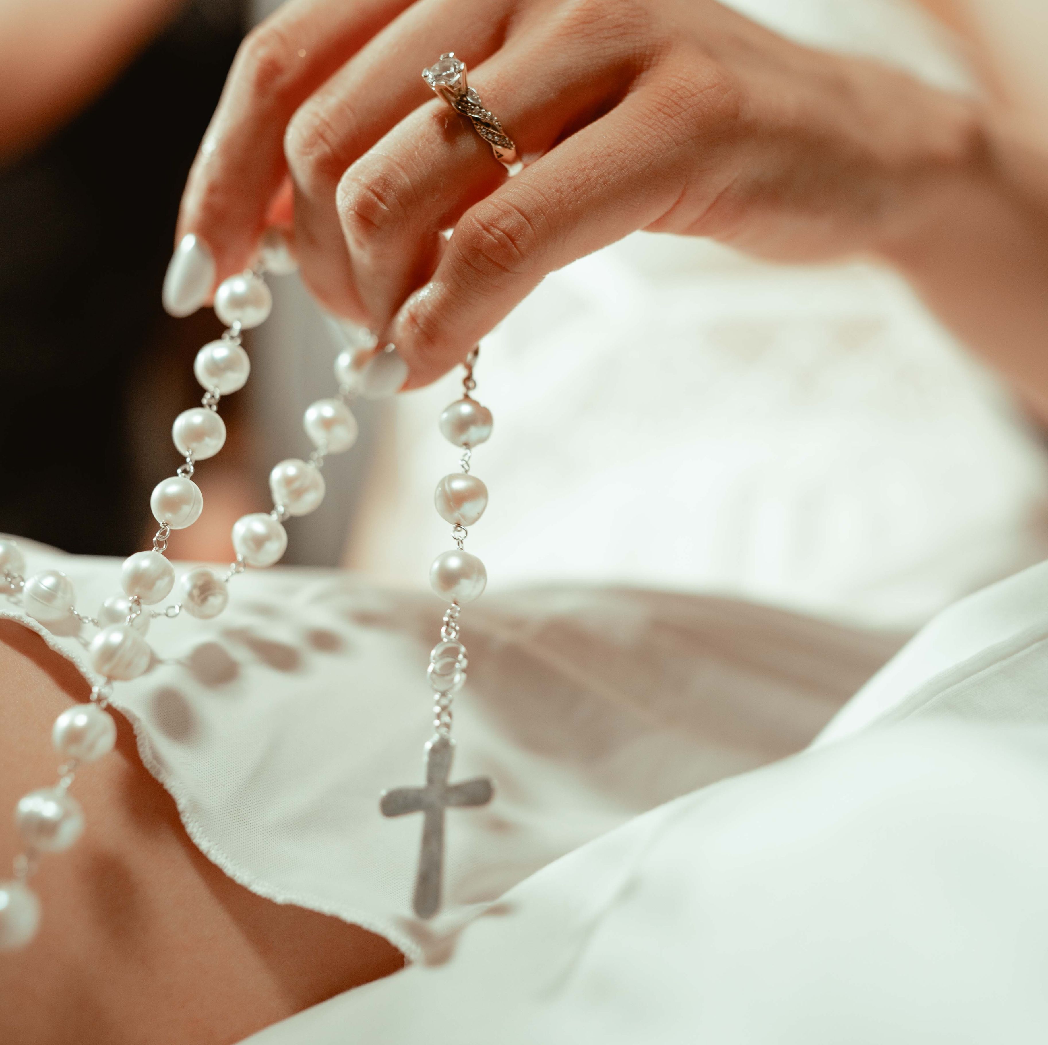 Ein weißer Rosenkranz mit einem silbernen Kreuz und zarten Perlen.