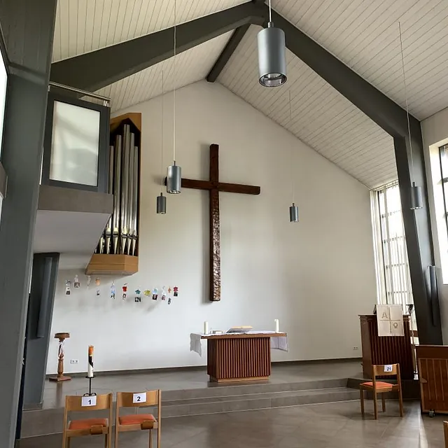 Kircheninneres mit großem Holzkreuz, Altar, Orgel und Stühlen.
