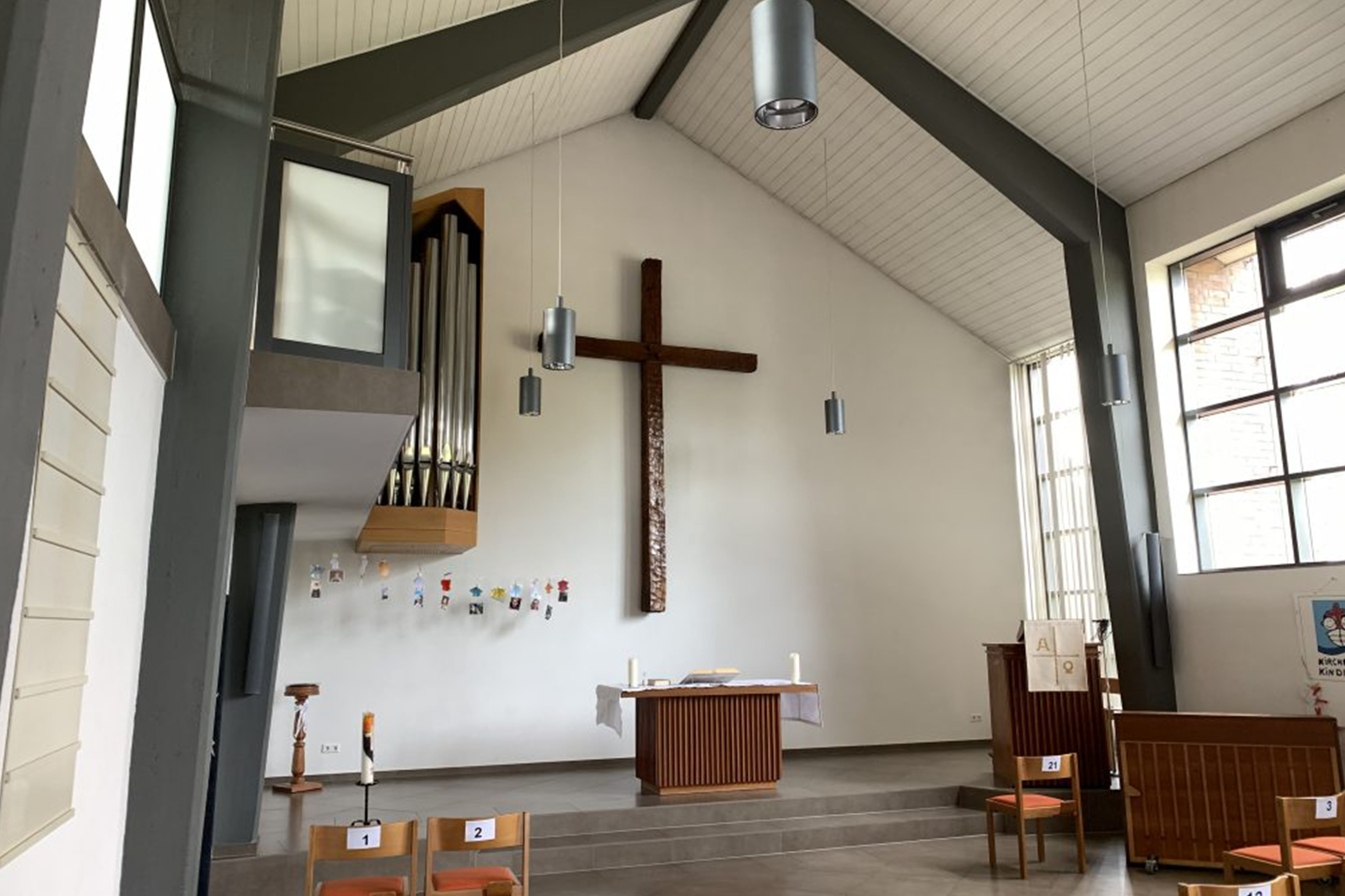 Moderner Kircheninnenraum: Großes Kreuz, Orgel, Altar, Stühle, Fenster.
