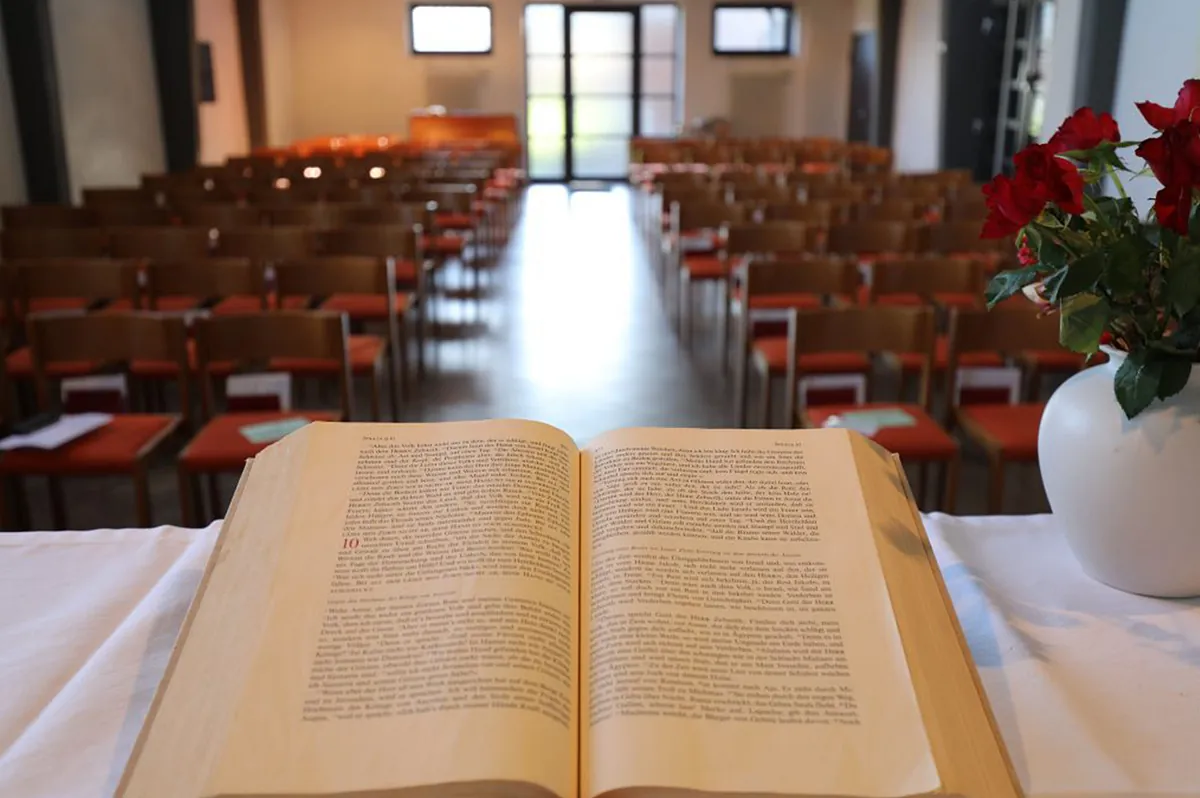 Offene Bibel auf Altar, mit roten Blumen, leere Kirchenbänke.