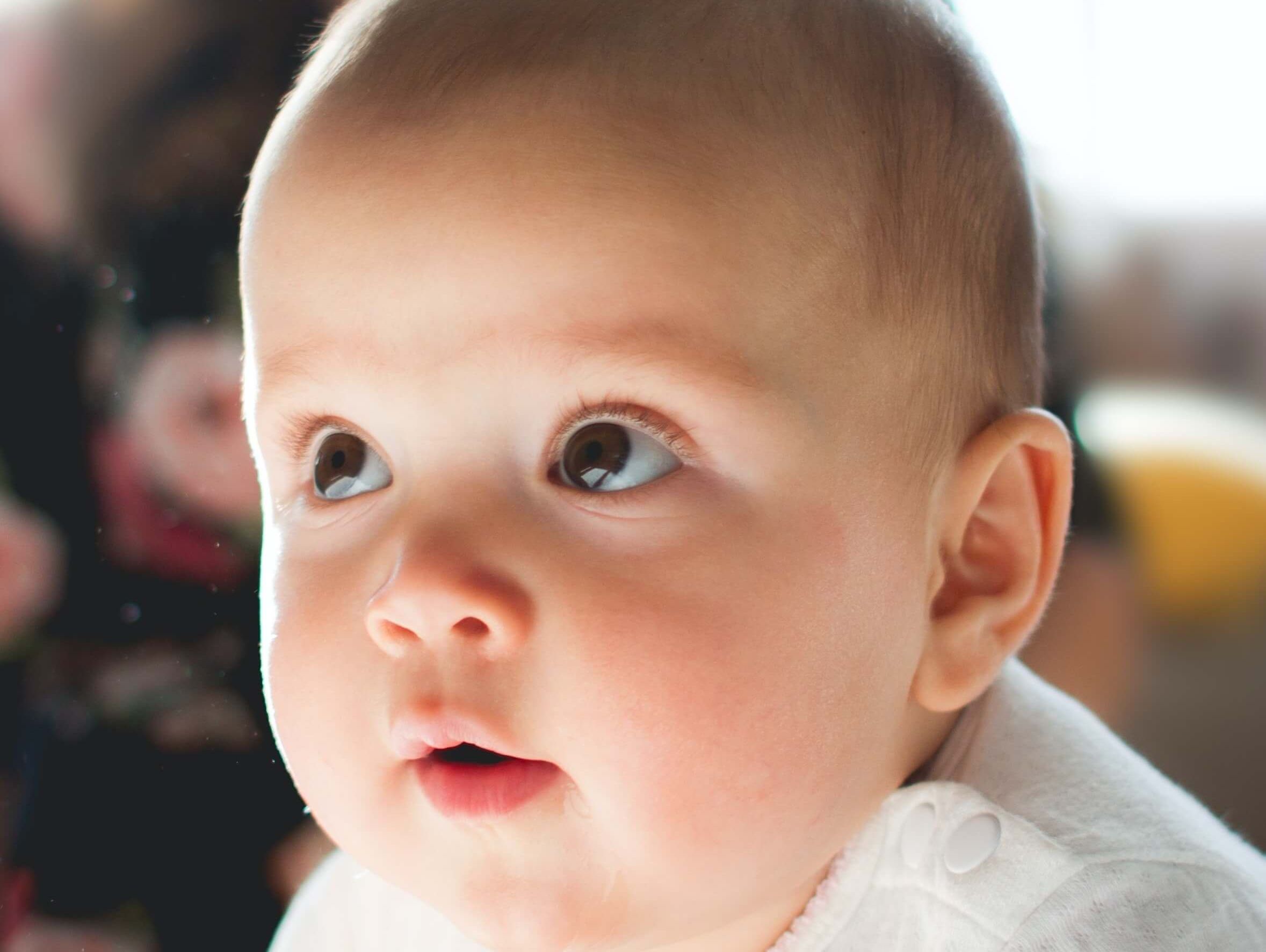Nahaufnahme eines Babygesichts mit großen, neugierigen, glasigen Augen.