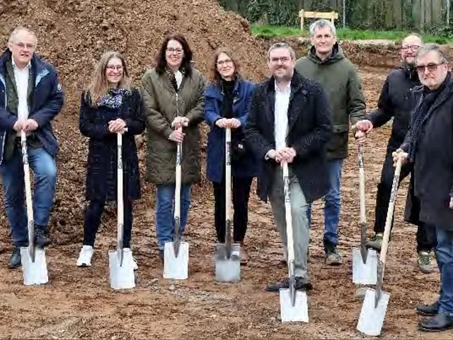 Gruppe Erwachsener mit Spaten bei einer Grundsteinlegung.