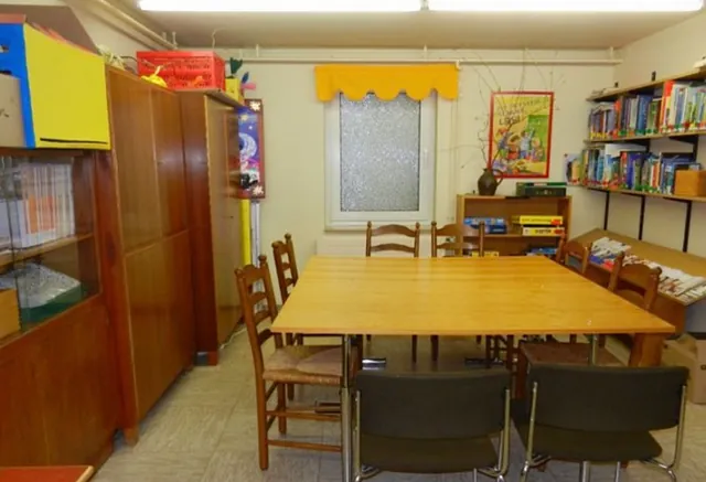 Gemeinschaftsraum mit großem Tisch, Stühlen, Bücherregalen, gemütliche Atmosphäre.