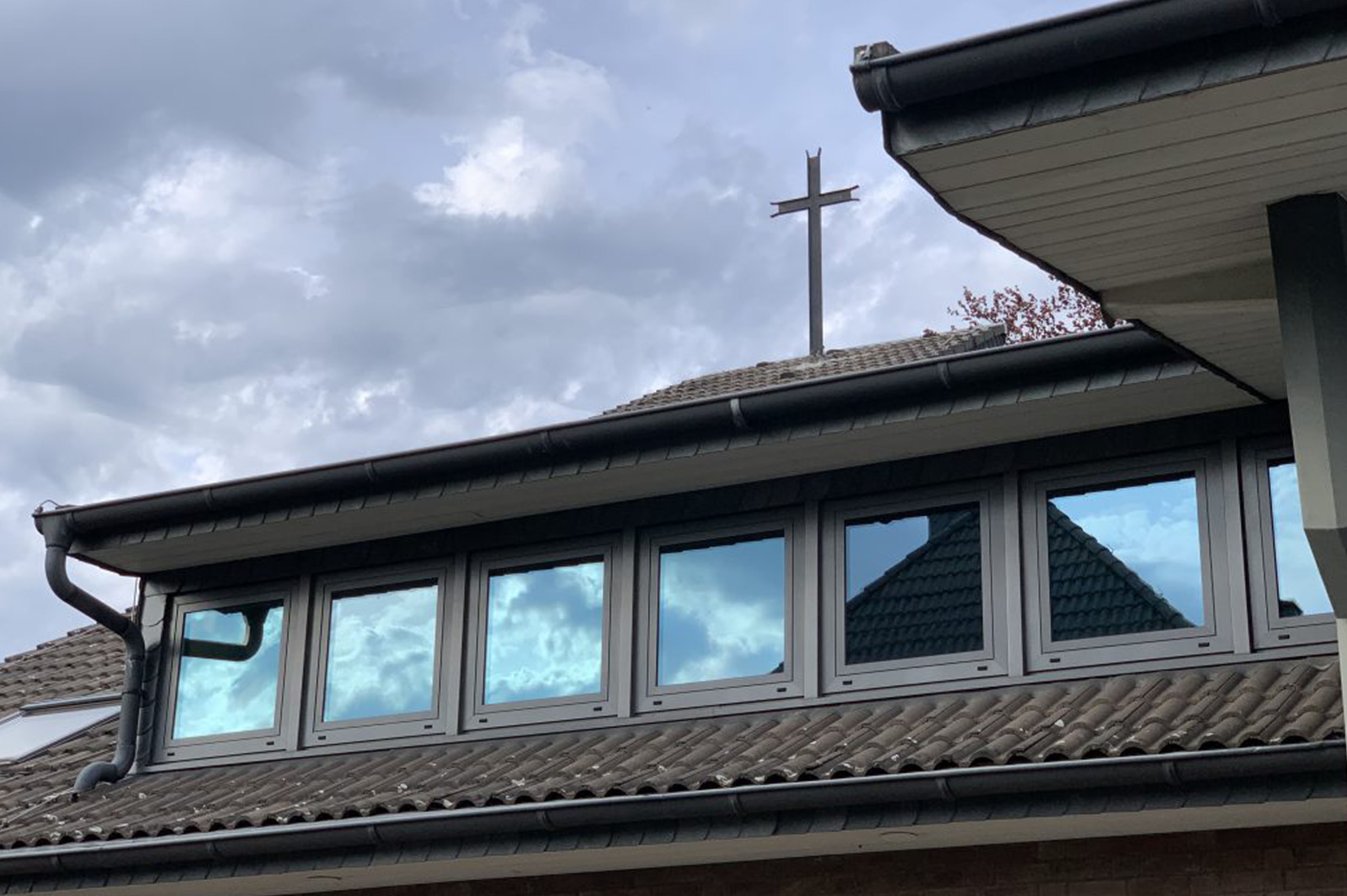 Kirchen dach mit Kreuz, Fenster spiegeln Himmel, und sichtbare Rinne.