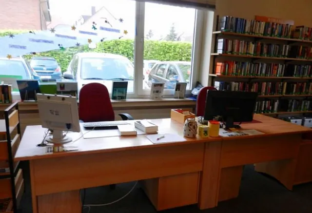 Bibliotheksausleihe, Computer, rote Stühle, Bücherregale, große Fensteransicht.