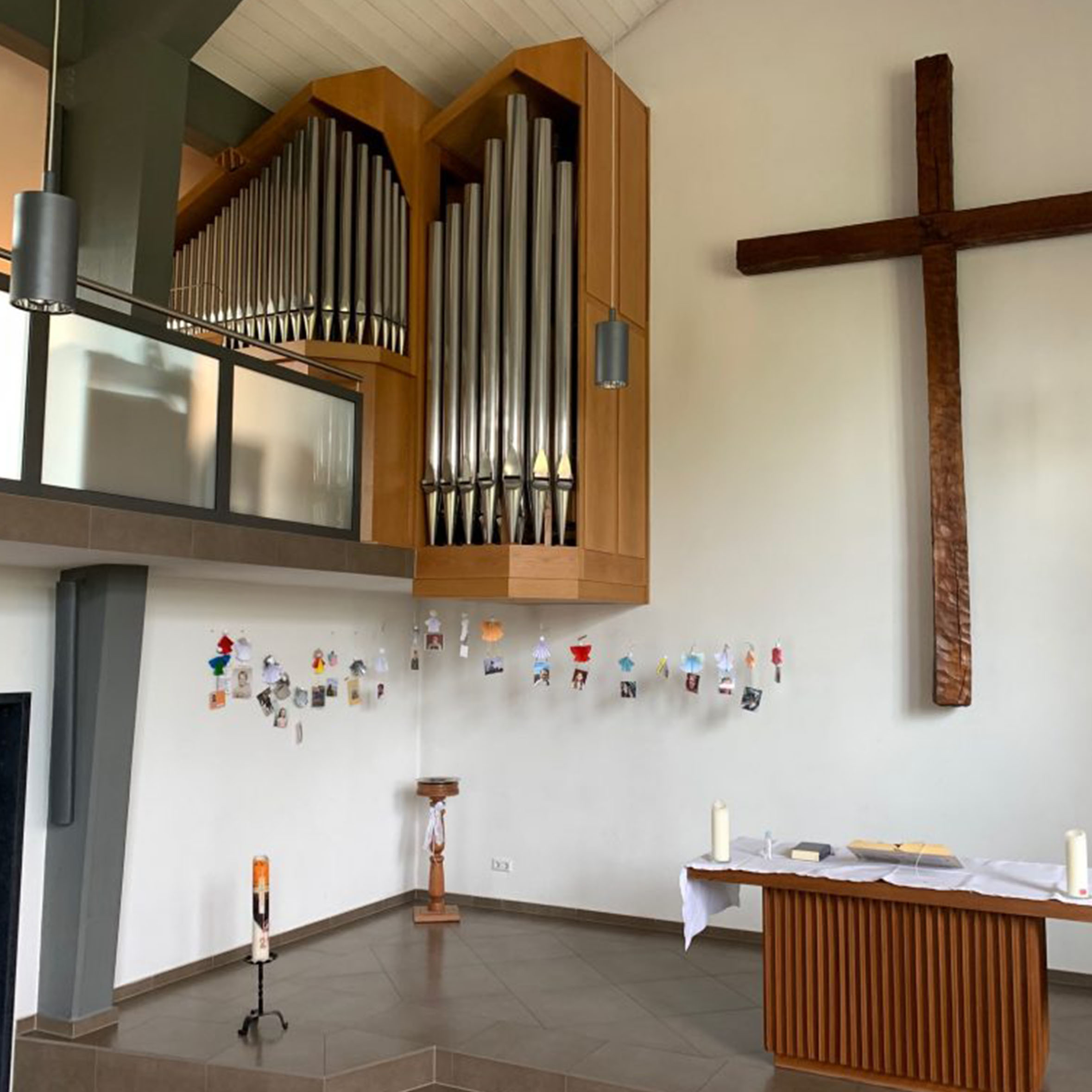 Kircheninnenraum: Großes Holzkreuz, Orgel, dekorierte Wand, Altar.