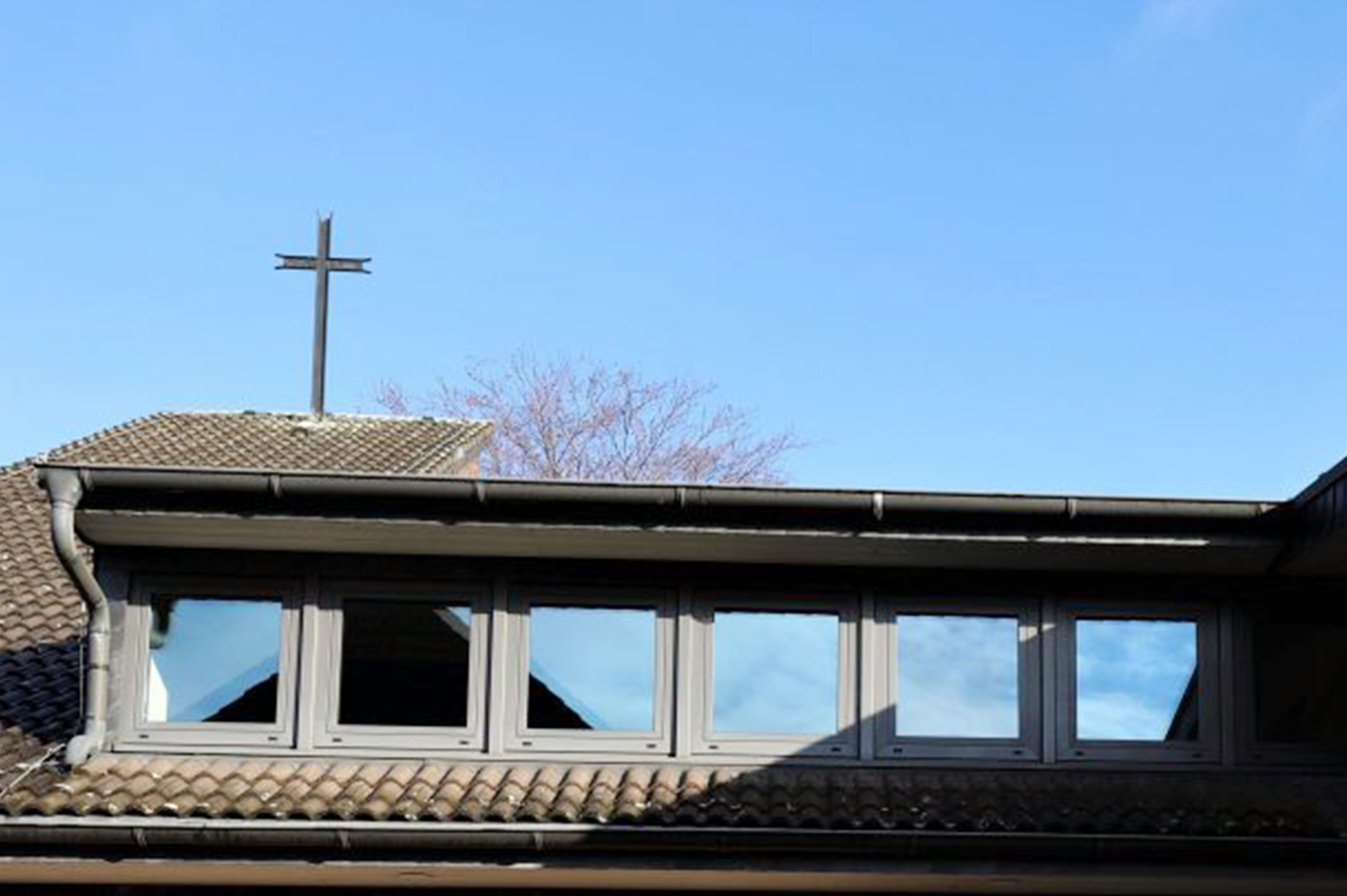 Dachgaubenfenster, spiegelnd, Kreuz, Kirchendach, klarer blauer Himmel.