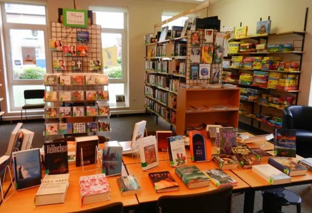 Bücher auf Tischen, Regalen, Bibliotheksinterieur, große Fenster, heller Raum.