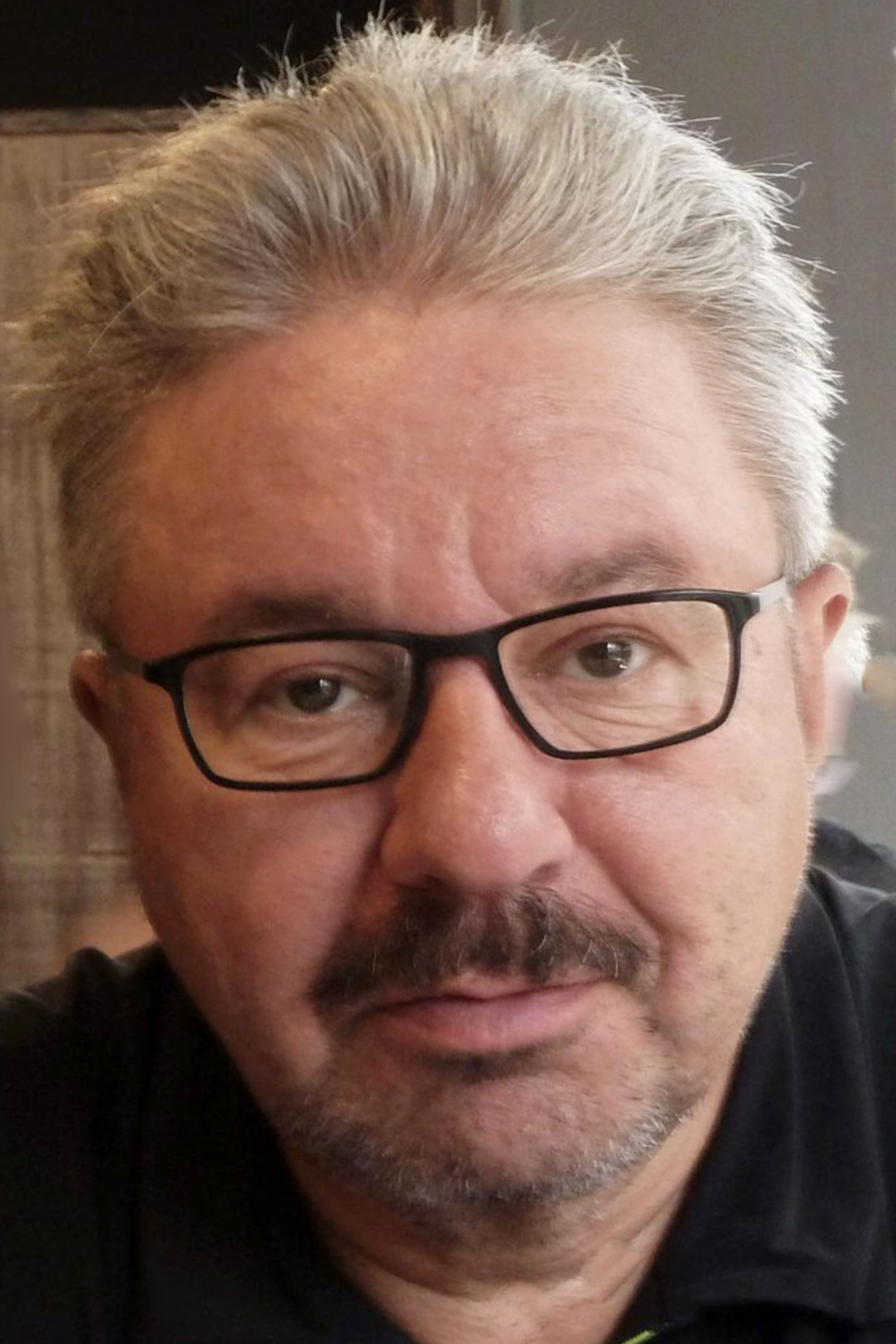 Porträt eines mittelalten Mannes mit Brille und Schnurrbart.