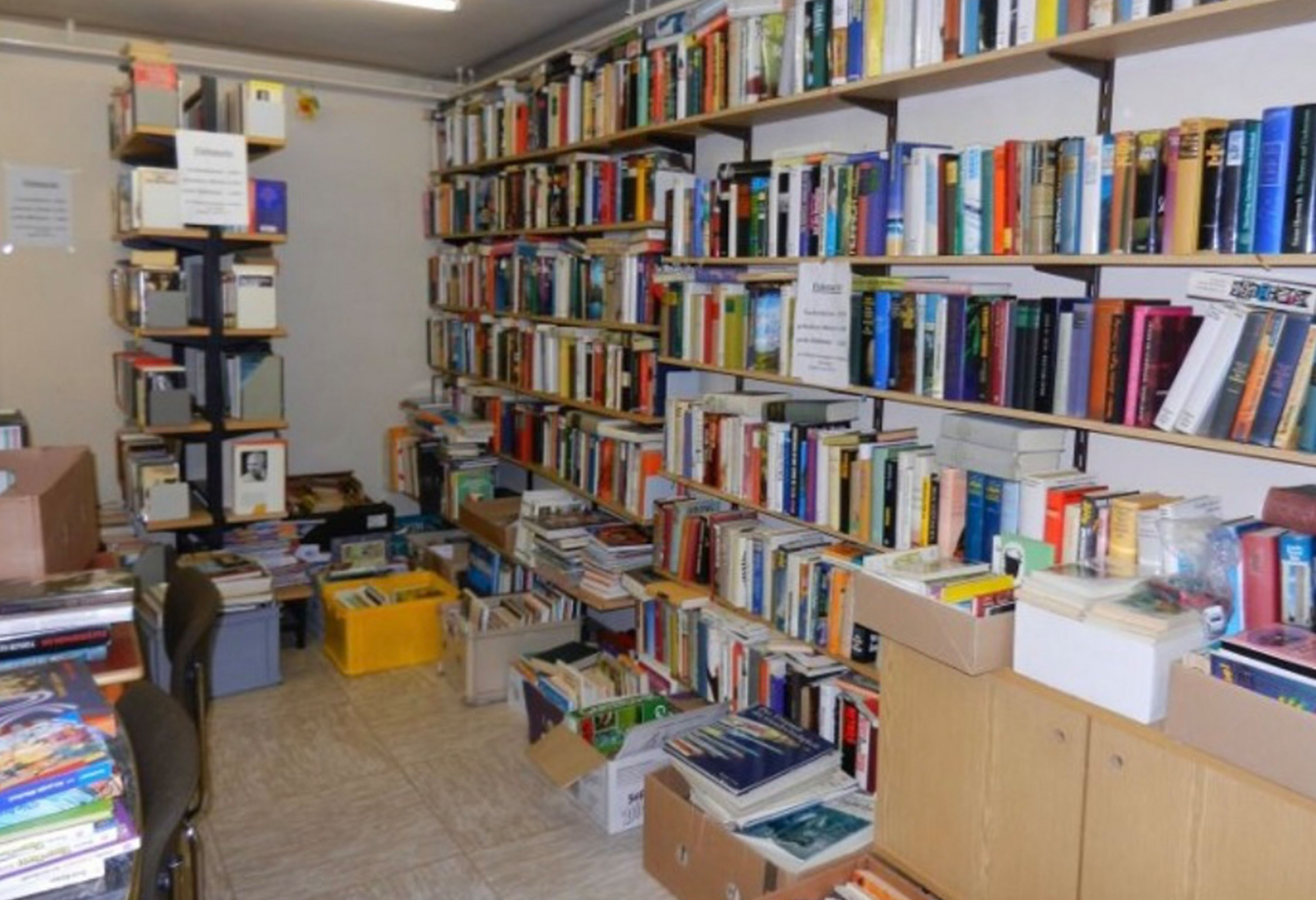 Überfülltes Buchhandlungsinterieur, überquellende Regale, Bücherstapel, literarisches Chaos.