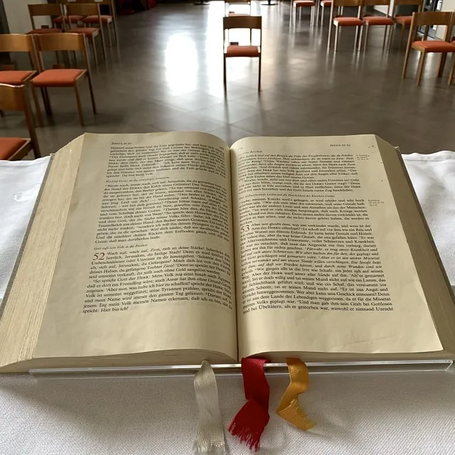 Offene Bibel, deutscher Text, Lesezeichen, Kirchenumgebung, Stühle.