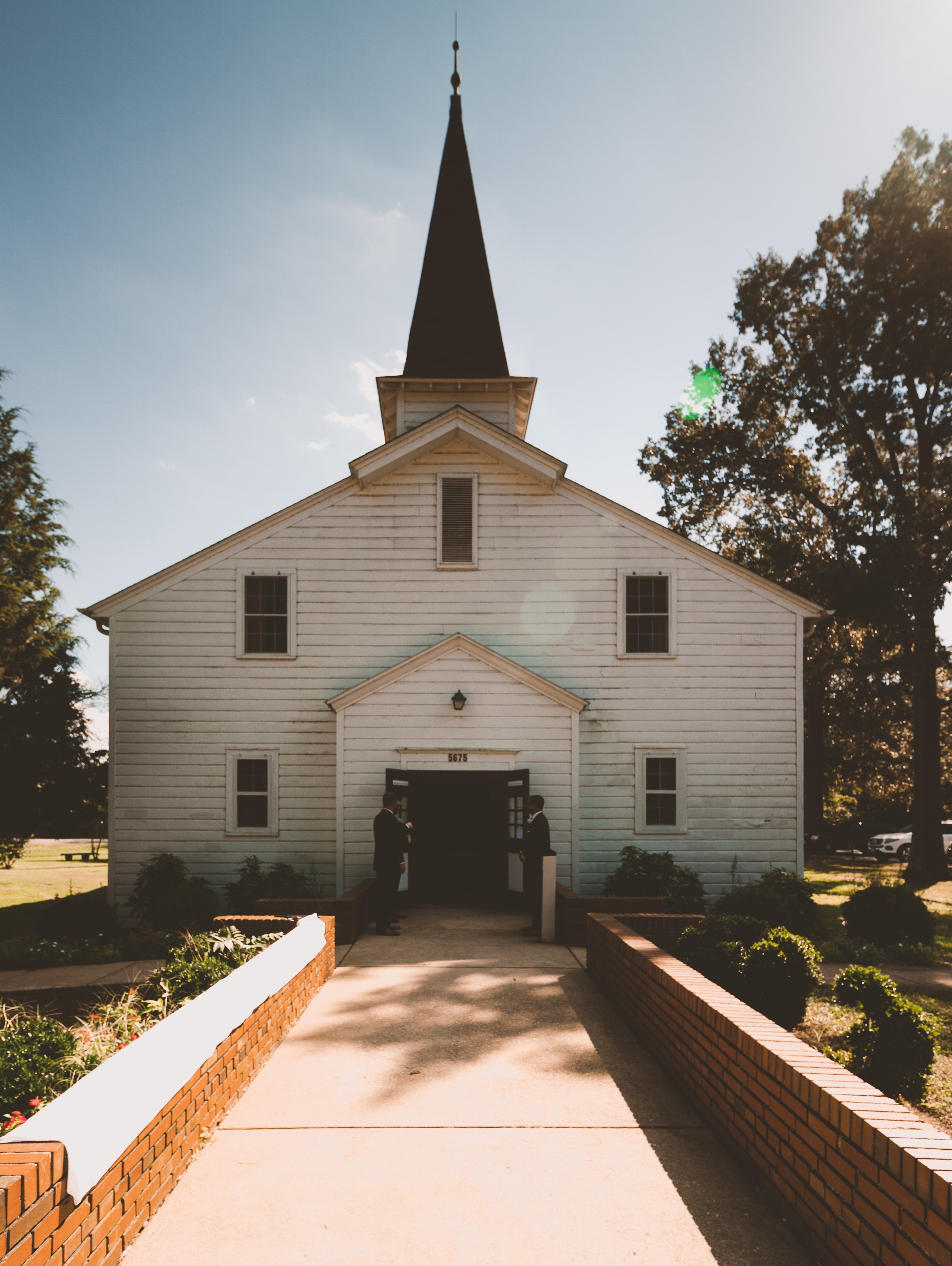 Ein Weg führt zu einer weißen Kapelle mit hohem, dunklem Turm.