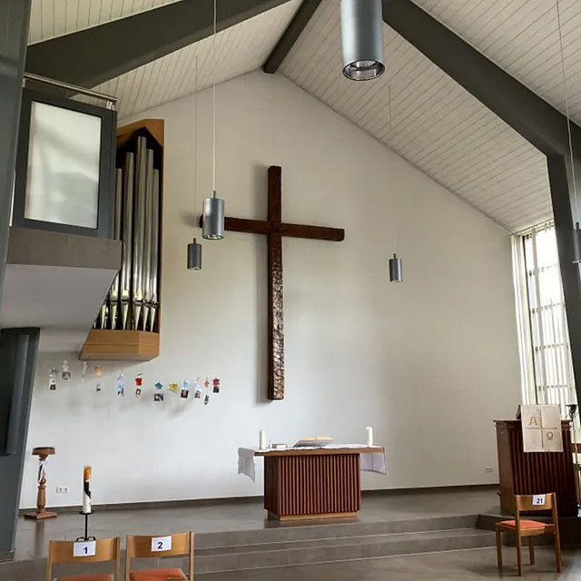 Moderner Kircheninnenraum mit großem Holzkreuz, Altar und Orgel.
