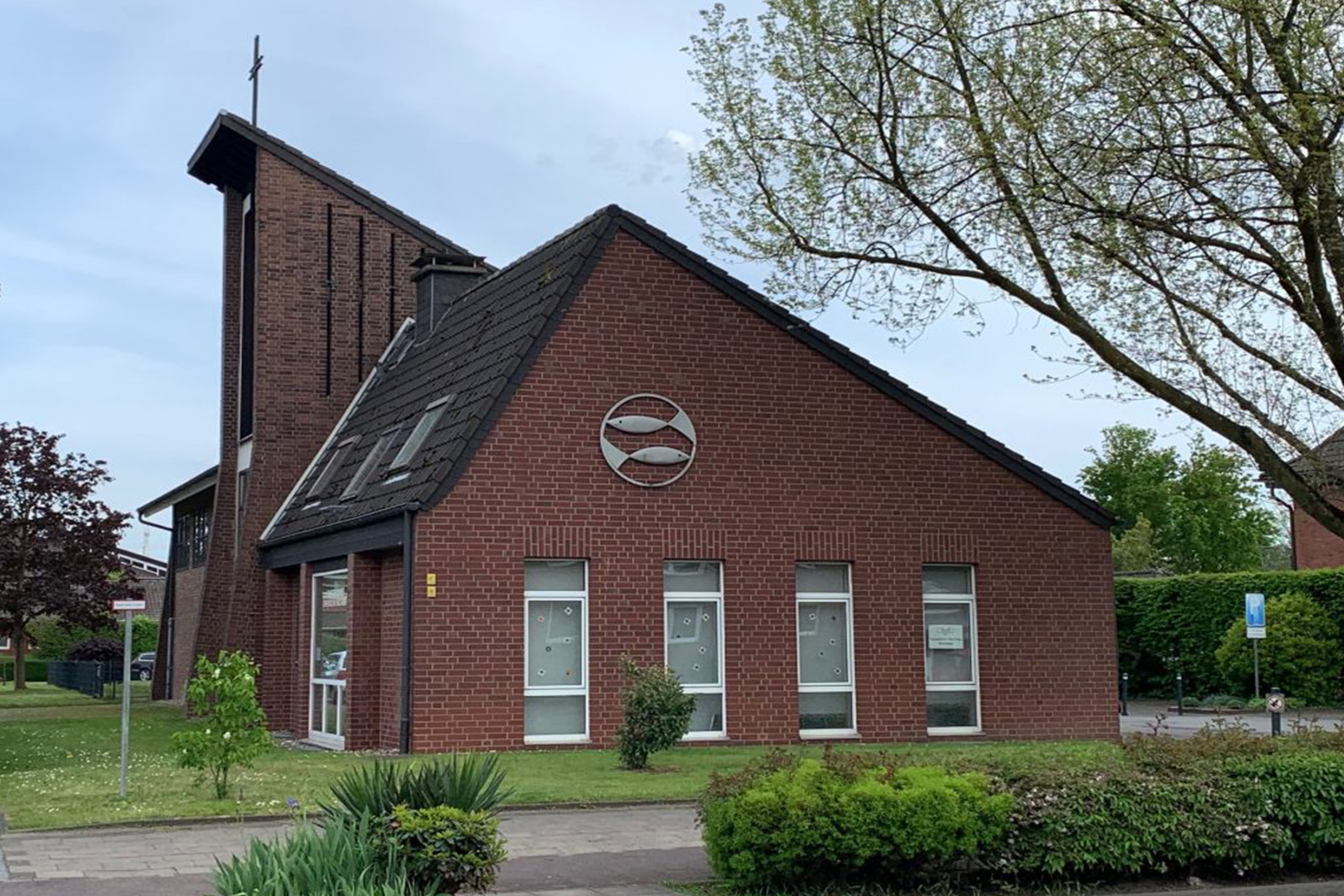 Backsteinkirche mit hohem Turm und Fischsymbol, grüne Umgebung.