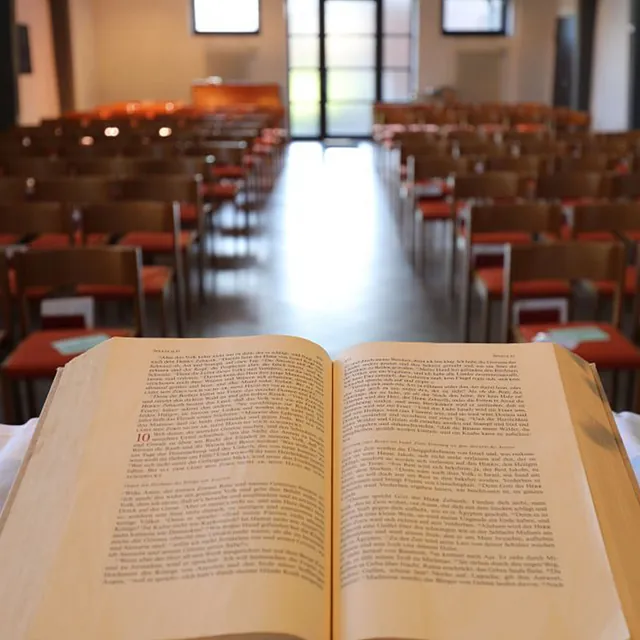 Offene Bibel im Fokus, Kirchenbänke im Hintergrund verschwommen.