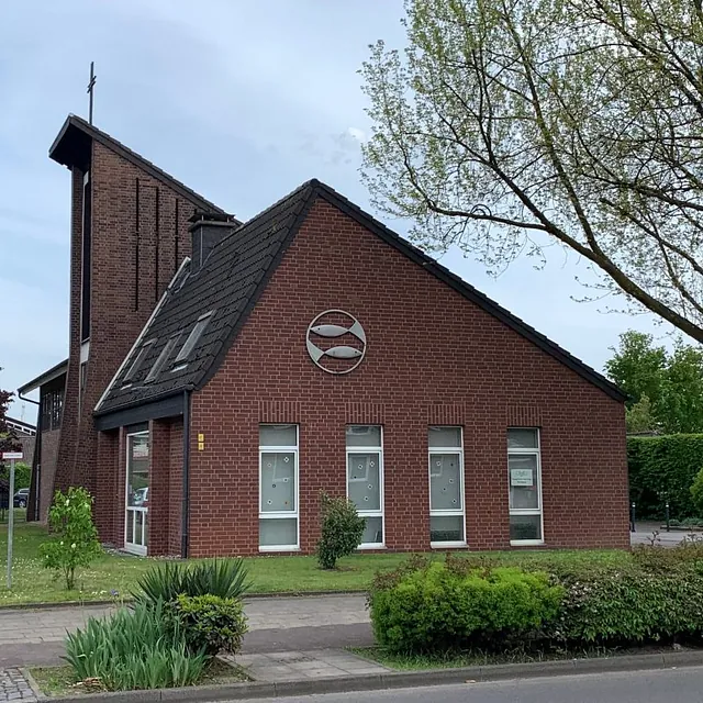 Backsteinkirche, Fischsymbol, Kreuz, moderne Architektur, grüne Umgebung.