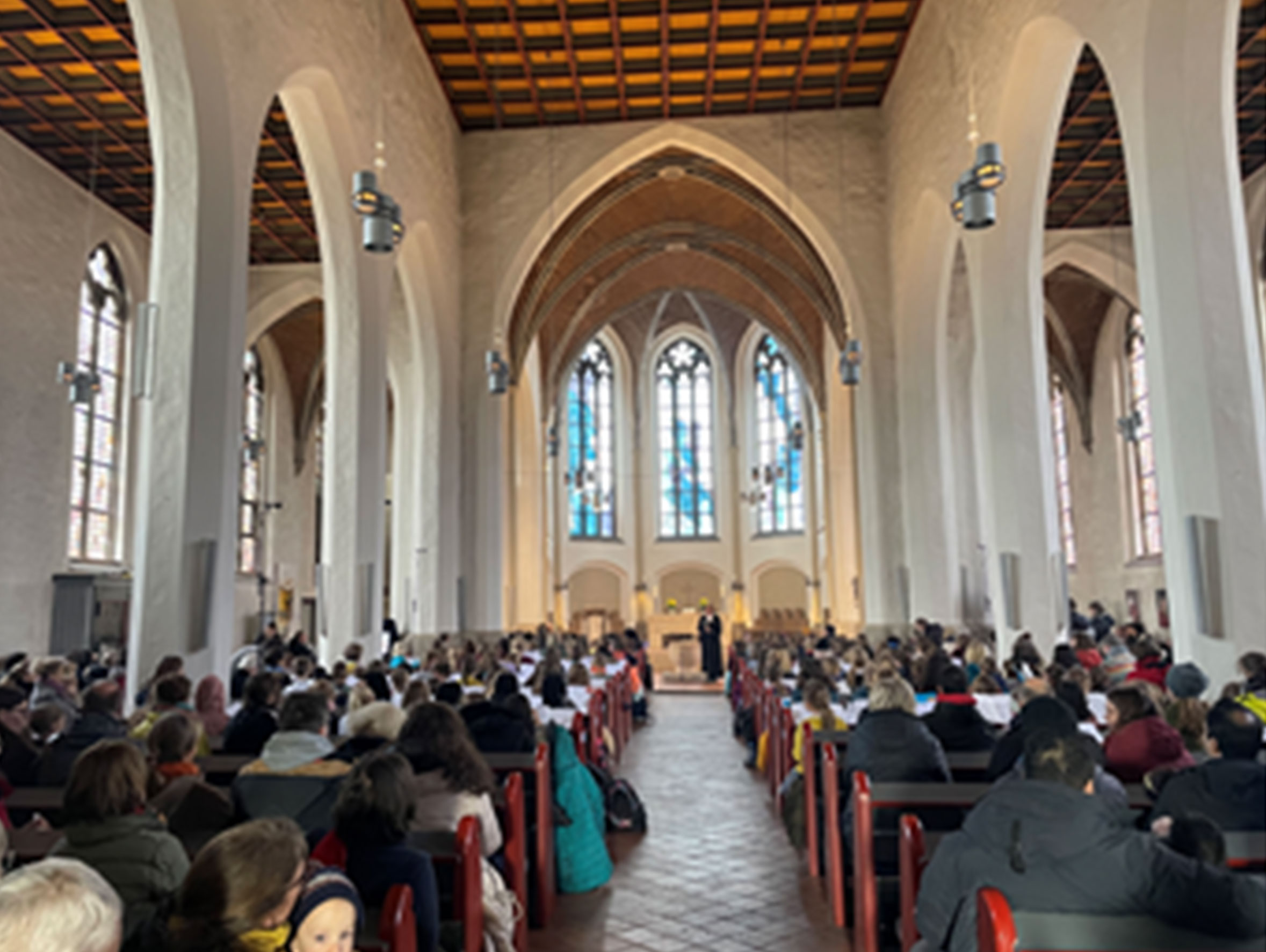 Großer Kircheninnenraum mit Gemeinde, hohen Decken, Buntglasfenstern.