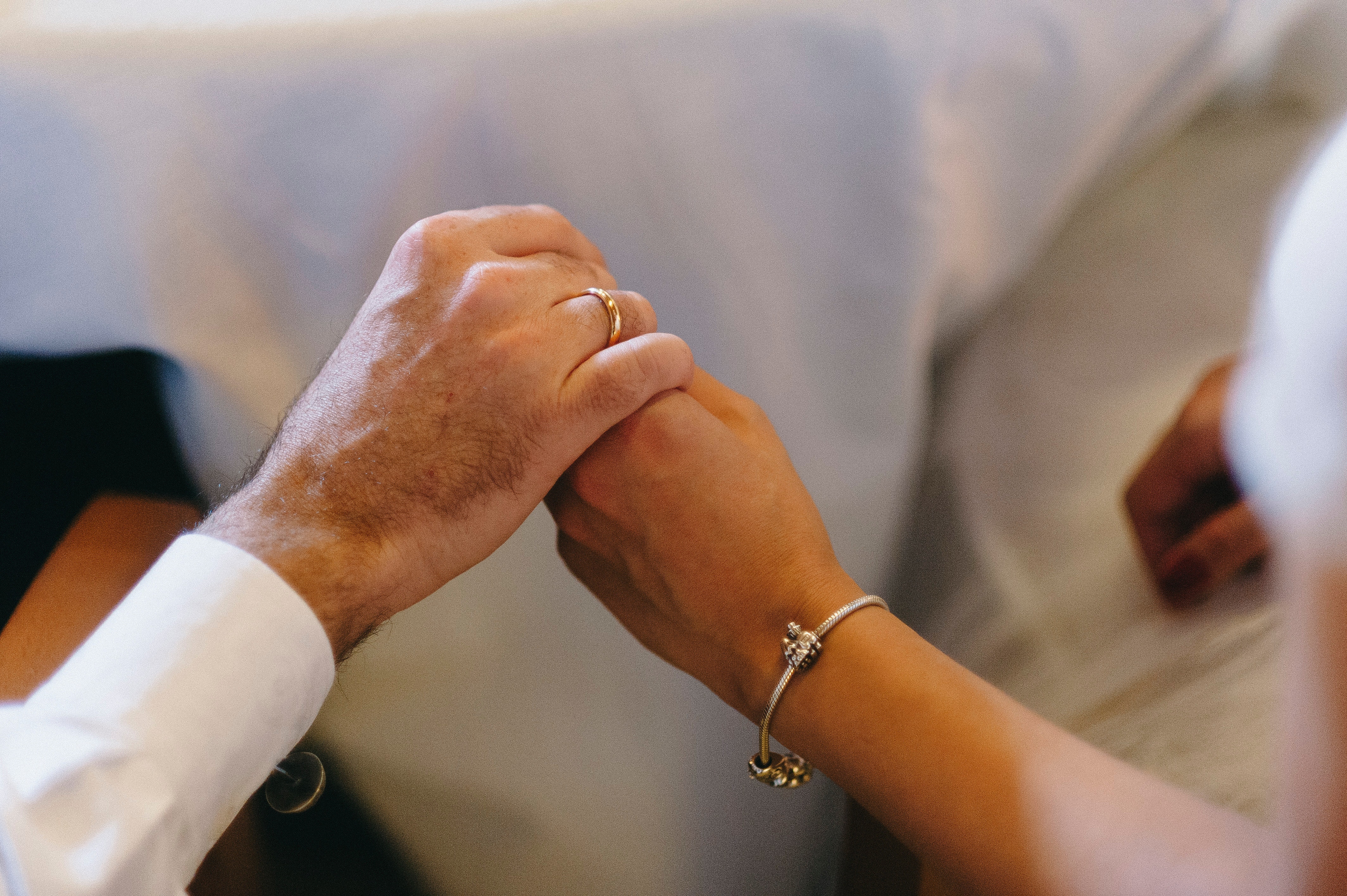 Verbundene Hände eines Paares, Eheringe im Sonnenlicht präsentierend.