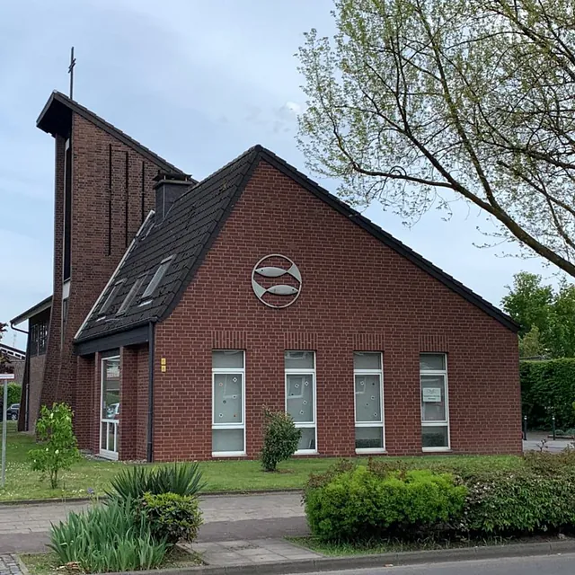 Moderne Backsteinkirche mit markantem Kreuz und Fischsymbol.