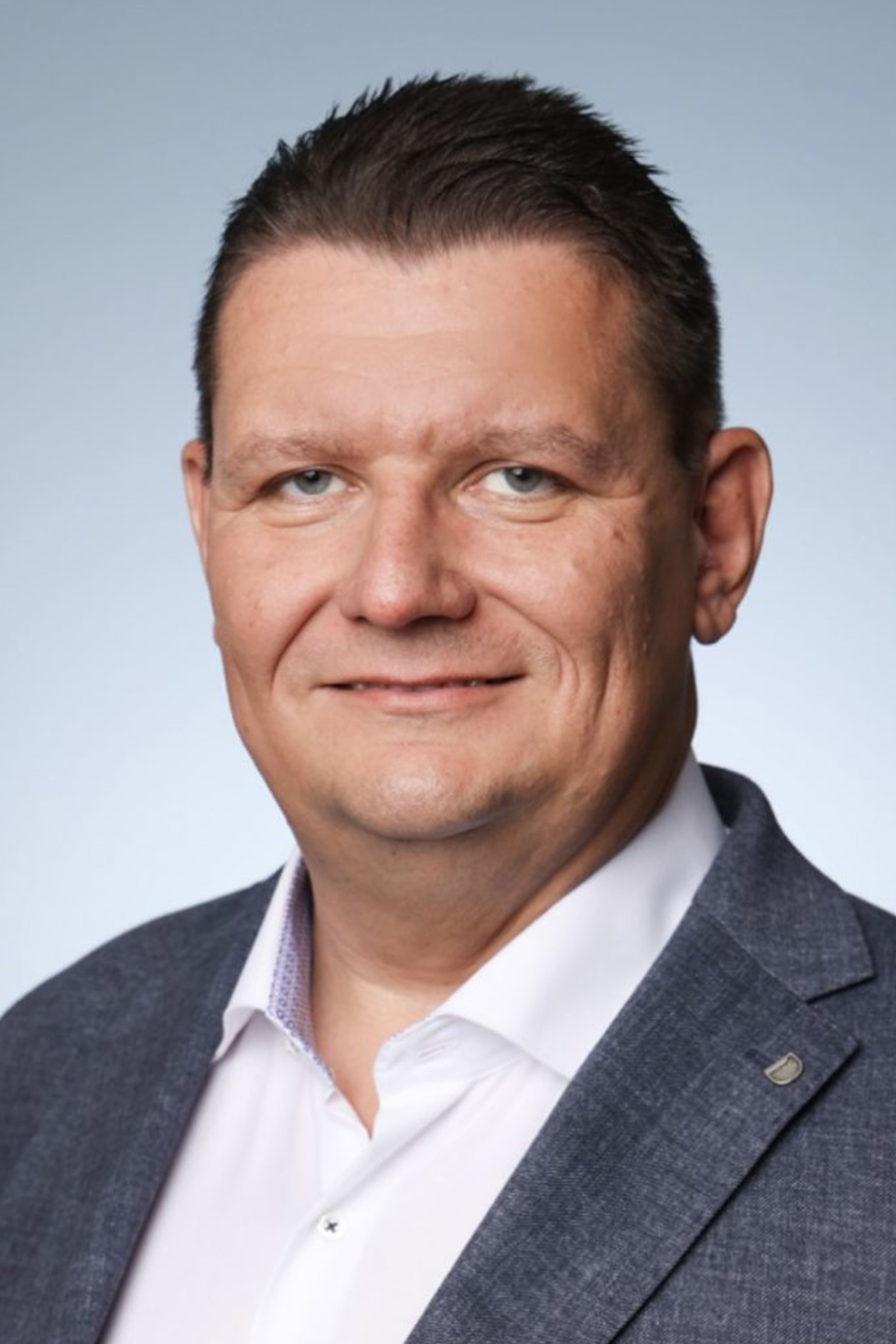 Professioneller Mann im Anzug lächelt, blickt direkt in Kamera.